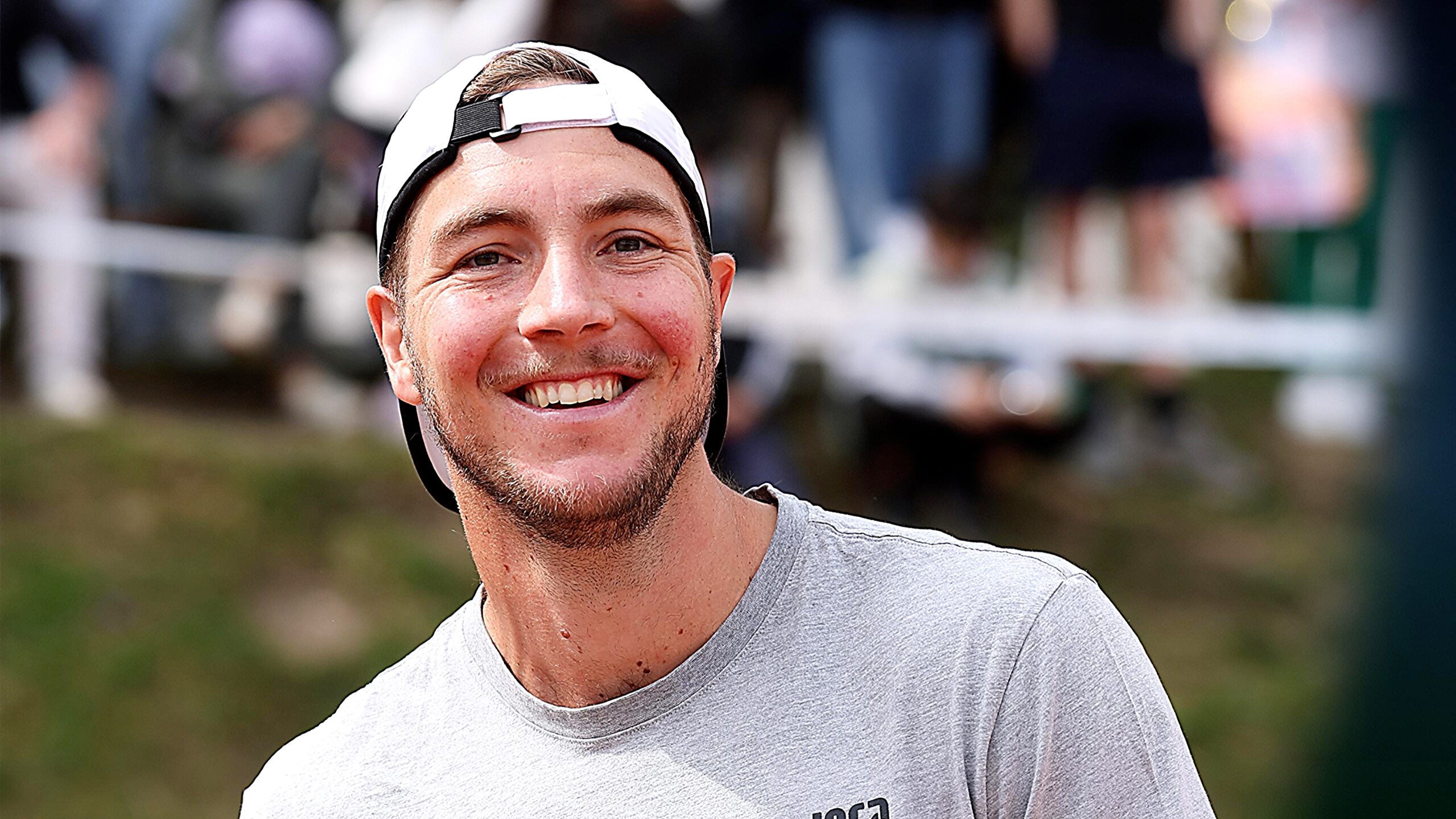 Jan-Lennard Struff hits a forehand during an ATP tennis match, wearing a white cap and black-and-yellow kit with a blurred stadium background